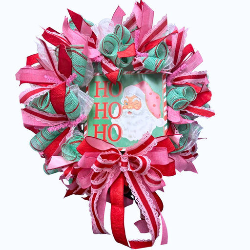The Mint Ho Ho Ho Christmas Completed Wreath features pink, green, and red ribbons around a sign with Santa Claus and the festive message Ho Ho Ho in green and red letters.