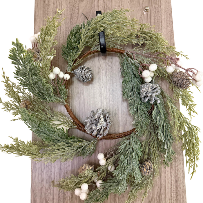 A 6.5 White Sparkle Soft Pine White Berry Ring (ISB78002) featuring pine branches, white berries, and a hint of sparkle hangs on a wooden door.