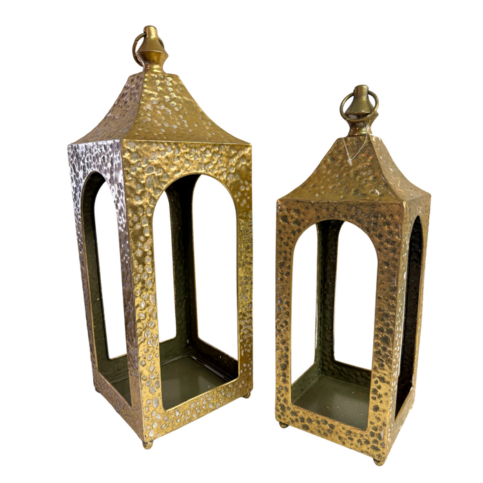 Two 20x6 and 16x5 Golden Hammered Metal Artisan Lanterns (M32600AB), each with arched openings and pointed tops, are displayed side by side against a white background; one lantern is taller than the other.