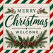 Merry Christmas Welcome red and green metal sign featuring striped border, pine, holly, red berries, and pinecone on a cream wood background. SKU TTE-574.