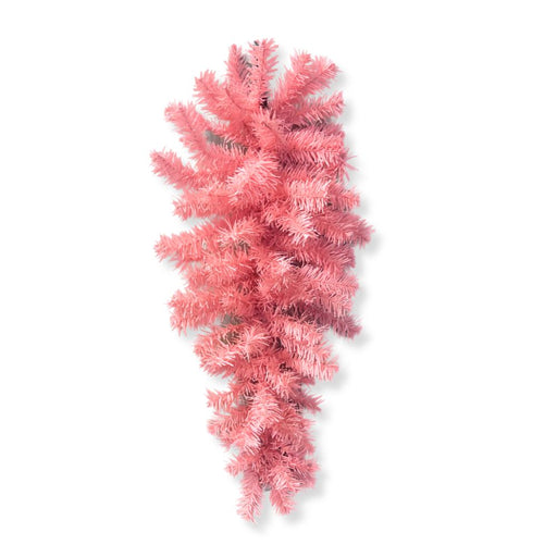 The 24" Pink Artificial Pine Teardrop Swag (82298-PK) features a cluster of pastel pink artificial pine branches elegantly arranged in a downward fan shape, creating a striking teardrop silhouette against a simple gray backdrop—ideal for adding seasonal charm to your decor.