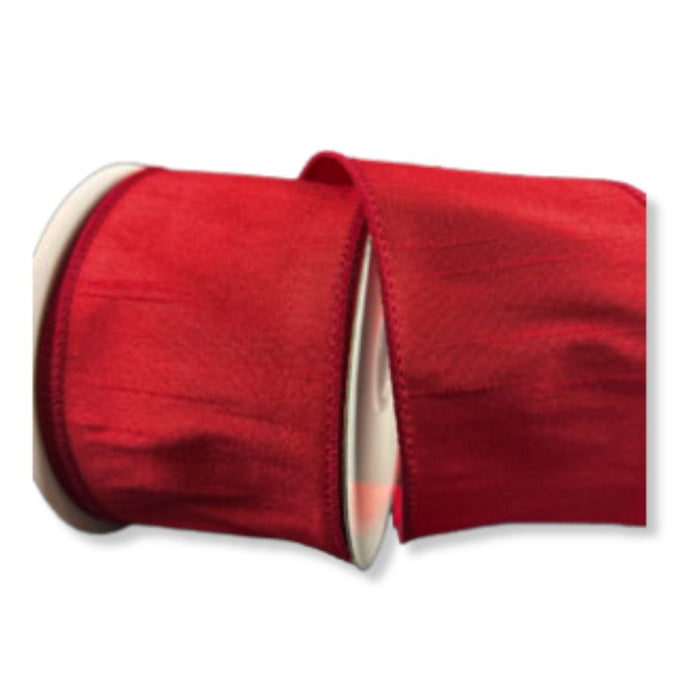 A spool of 2.5" Red Faux Dupioni Wired Ribbon (72434-40-12) is partially unrolled, highlighting its smooth, shiny texture and silk-like finish. The wired ribbon features finished edges and is set against a white background.