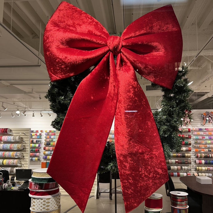 Oversized red velvet 3D Christmas hanging bow measuring 32 by 47 inches with long tails.