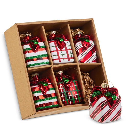 The Set of 6 Striped & Plaid Gift Box Glass Ornaments (RAZ 4522921) features six festive ornaments in classic red, white, and green striped and plaid patterns, neatly arranged in a brown divided cardboard box. Crafted by RAZ Imports, these charming glass ornaments are perfect for decorating your Christmas tree. One ornament is showcased outside the box in the foreground.