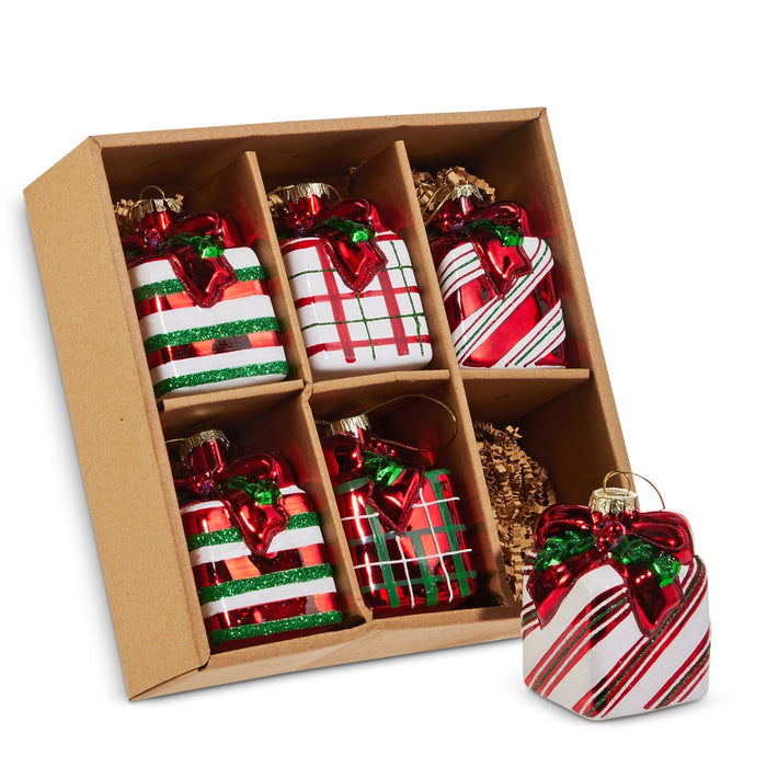The Set of 6 Striped & Plaid Gift Box Glass Ornaments (RAZ 4522921) features six festive ornaments in classic red, white, and green striped and plaid patterns, neatly arranged in a brown divided cardboard box. Crafted by RAZ Imports, these charming glass ornaments are perfect for decorating your Christmas tree. One ornament is showcased outside the box in the foreground.