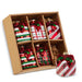 The Set of 6 Striped & Plaid Gift Box Glass Ornaments (RAZ 4522921) features six festive ornaments in classic red, white, and green striped and plaid patterns, neatly arranged in a brown divided cardboard box. Crafted by RAZ Imports, these charming glass ornaments are perfect for decorating your Christmas tree. One ornament is showcased outside the box in the foreground.