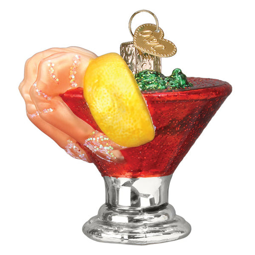 The Shrimp Cocktail Ornament by Old World Christmas (32507) features a glittery hand holding a red cocktail glass reminiscent of shrimp cocktail, complete with faux lemon slice, metallic base, and shiny red liquid. It includes a gold loop for hanging, perfect for ocean lovers.