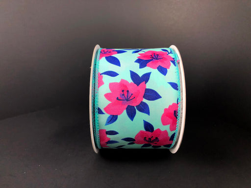The 2.5X10Y Aqua Satin/Fuchsia Magnolias Ribbon features a floral design with pink flowers and dark blue leaves on an aqua satin background against a dark backdrop.