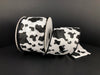 The 2.5X10Y White Linen/Black Cow Print Ribbon 41343-40-21 features a striking black and white cow pattern on a dark backdrop with a wired edge to maintain its form when unrolled, showcasing the unique design.