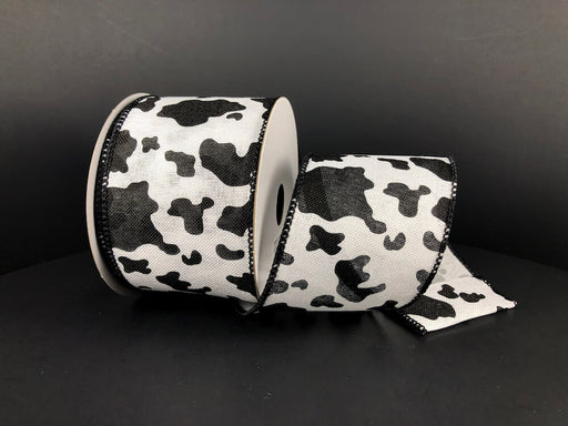 The 2.5X10Y White Linen/Black Cow Print Ribbon 41343-40-21 features a striking black and white cow pattern on a dark backdrop with a wired edge to maintain its form when unrolled, showcasing the unique design.