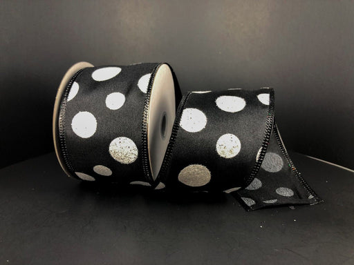 A partially unwound reel of Black Satin/White Glitter Big Dots ribbon, measuring 2.5x10Y (75104-40-21), sits against a dark background, showcasing its synthetic sheen and evenly spaced large white polka dots for striking contrast.