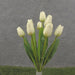 A bouquet labeled as 16 Tulip Bush Cream With 9 Stems SB2375-CRM showcases cream tulips with lush leaves against a gray background, elegantly arranged in a white vase and highlighted by a strip of green grass at the bottom.
