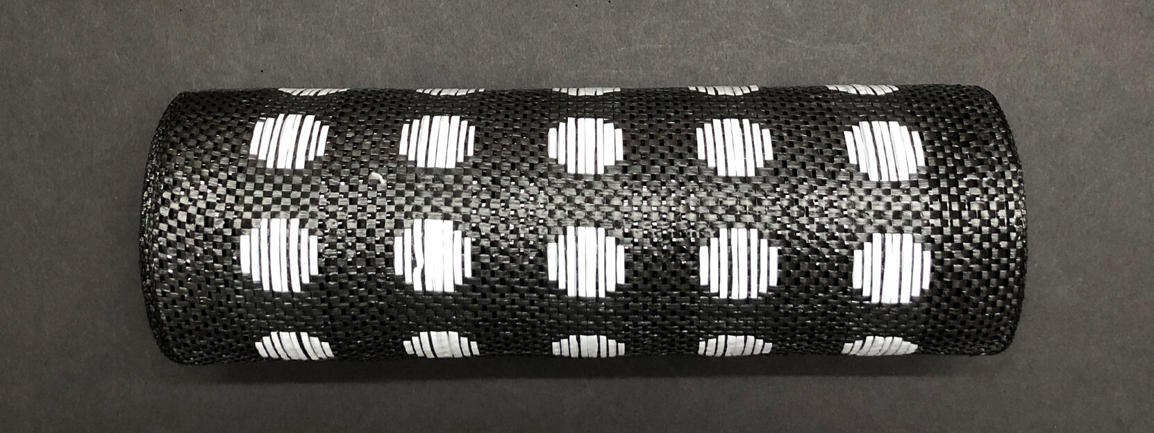 The Polka Dot Black-White Woven Mesh, 10X10Y Mesh XB108410-21, a cylindrical object with a black textured surface and evenly spaced white polka dots, is placed on a dark background.