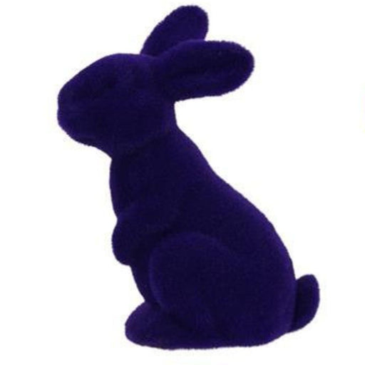 An 11.5"H x 7"L flocked sitting rabbit figurine, seen in assorted colors like purple, pink, black, green, turquoise, and orange (HE723099), sits upright and faces left against a plain white background.