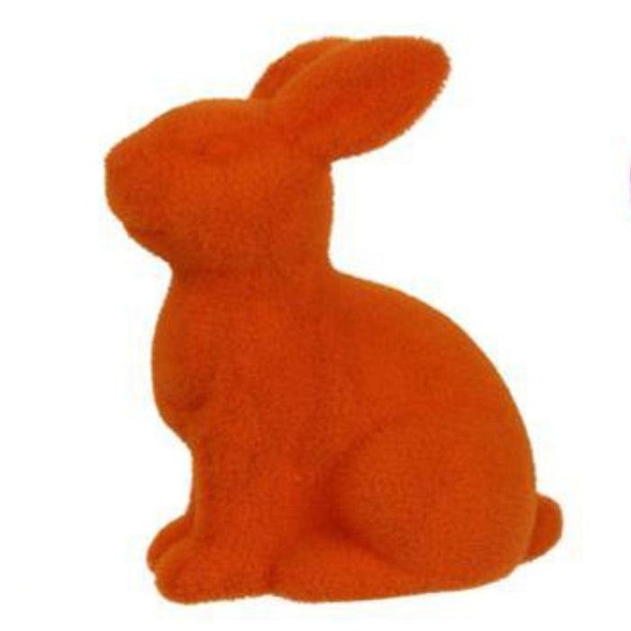 The 10H x 8.25L Flocked Sitting Rabbit, available in assorted colors including orange, features a fuzzy texture and is crafted from polystyrene. It sits facing left against a white background. Product code: HE723199.