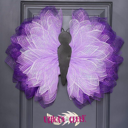 A butterfly-shaped decorative wreath crafted on a Plastic Insect Butterfly Body Board, featuring layered mesh wings in purple and lavender shades, adorns a dark door with Unique in the Creek inscribed at the bottom.