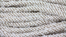Close-up of coiled Deco Flex Tubing Snowdrift RE3221CC. It displays a fuzzy, braided texture with white and beige hues, showcasing the intricate fiber weave—ideal for elegant gift wrapping.