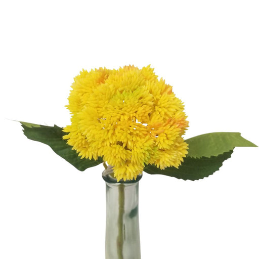The 15 Yellow Sedum Stem SB6323-YEL features a vibrant round cluster of yellow sedum with hints of orange, elegantly arranged in a clear vase with green leaves subtly tucked behind, all set against a pristine white background.