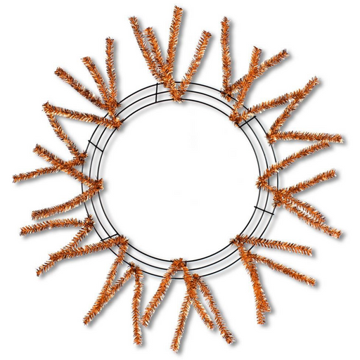 The Pencil Work Wreath 24 Metallic Copper XX751138 features a sunburst design with orange tinsel branches on a circular metallic copper frame. Its minimalist style leads to an open and airy arrangement, centered around the decorative outer structure.