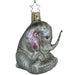 The Playful Pachyderm Elephant Christmas Ornament by Inge-Glas of Germany (1-136-02) is a charming glass treasure shaped like a sitting elephant with its trunk raised, featuring shiny details like rhinestones on the ears and feet, and a gold star-shaped hanging loop.
