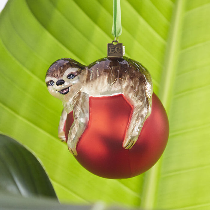 A RAZ Sloth on Red Ball Christmas Ornament featuring a sloth hanging onto a round, red ball.