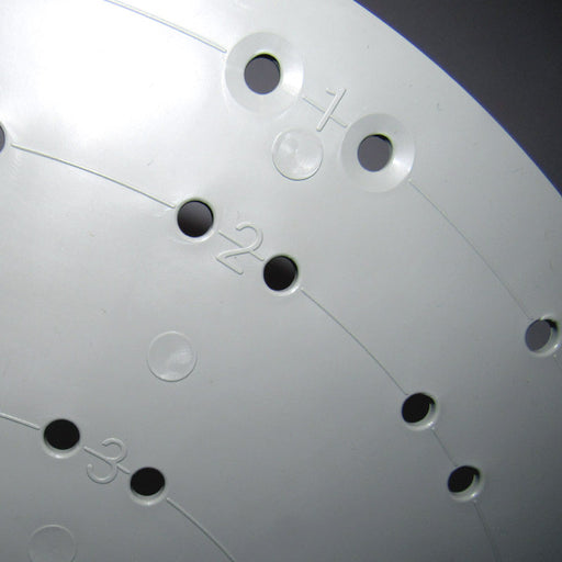 A close-up of a white circular plastic disc shows numbered sections and multiple holes, reminiscent of a 15.5 Plastic Flower Wreath Form. Numbers 1, 2, and 3 are visible beside the holes, indicating it might be part of a dial or rotary mechanism.