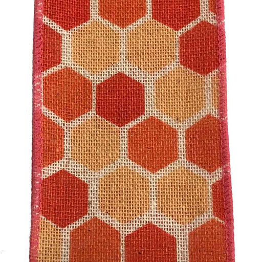 The 2.5 Ivory Canvas Coral Hex Ribbon Q814840-23 showcases a close-up of a rectangular fabric with a honeycomb pattern featuring hexagons in orange and red shades. Red-stitched canvas ribbon edges enhance the design, set against a burlap-like background texture.